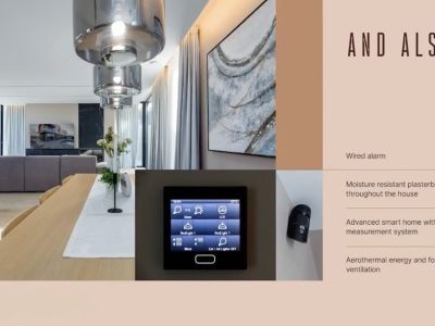 Salón-comedor de diseño abierto con mesa de madera, lámparas colgantes y panel de control domótico integrado, junto a un sensor de seguridad.