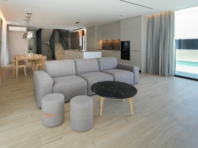 Salón-comedor de diseño abierto con sofá modular, mesa de mármol y cocina integrada, conectado a la piscina exterior a través de amplios ventanales.