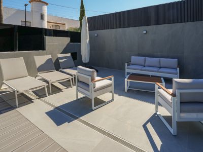 Terraza exterior con mobiliario de diseño en tonos neutros, combinando gres porcelánico y tarima de composite. Incluye tumbonas y zona de estar con sofá y sillones.