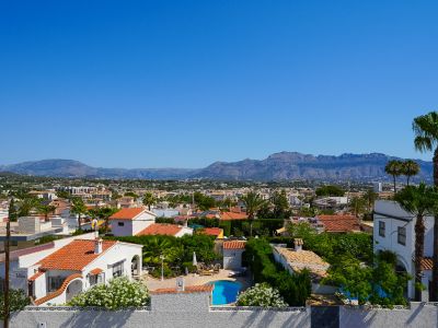 Vista elevada del entorno residencial de Albir, destacando una piscina privada, casas con tejados de teja y exuberante vegetación mediterránea, con montañas al fondo.