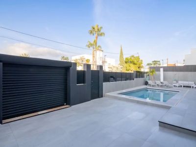 Vista exterior con piscina privada, patio de baldosas claras y puerta de garaje oscura con acceso peatonal seguro.