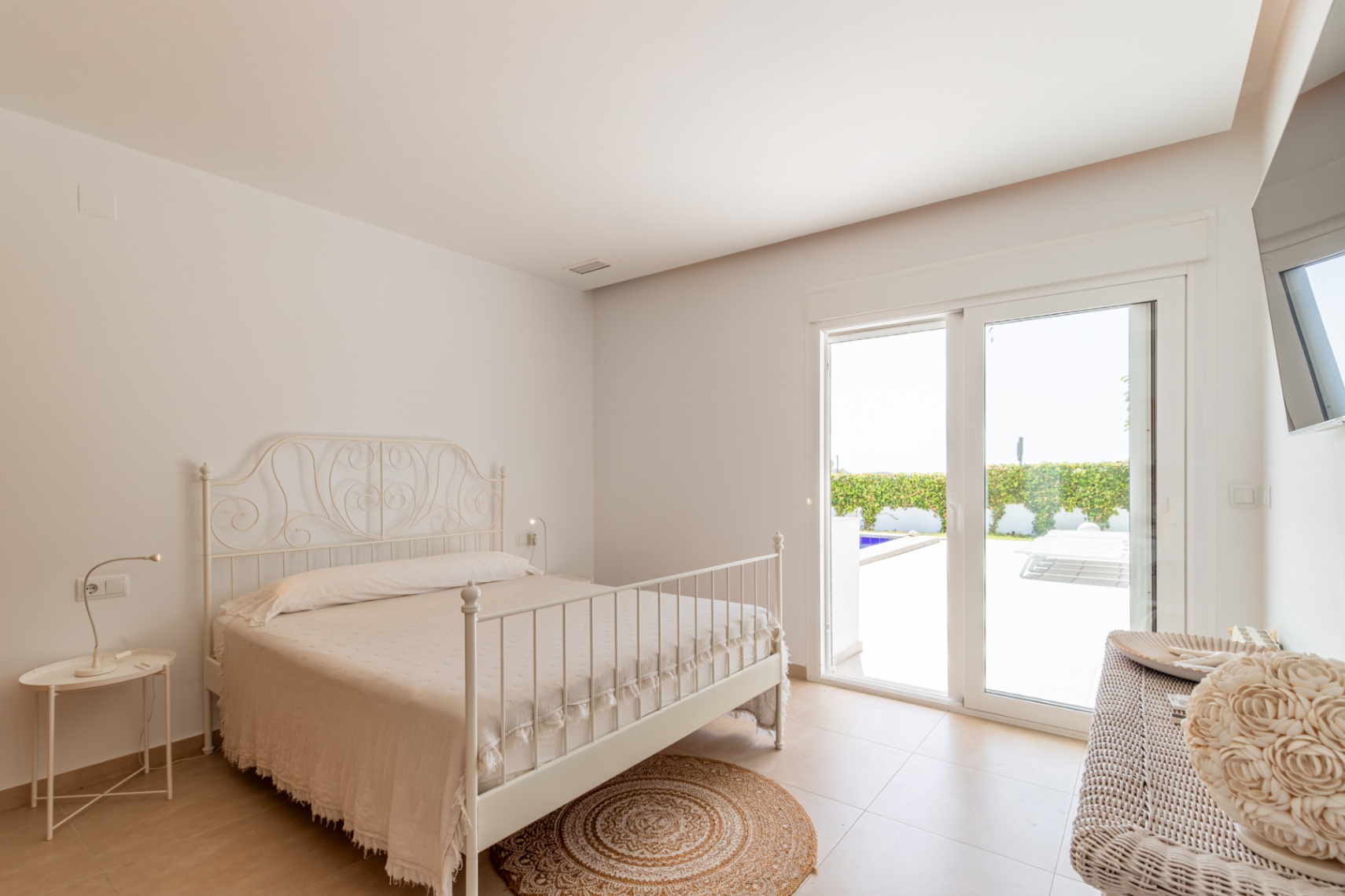Dormitorio luminoso con cama de forja blanca, suelo cerámico y acceso directo a la terraza exterior con vistas a la piscina. Dormitorio luminoso con cama de forja blanca, suelo cerámico y acceso directo a la terraza exterior con vistas a la piscina.