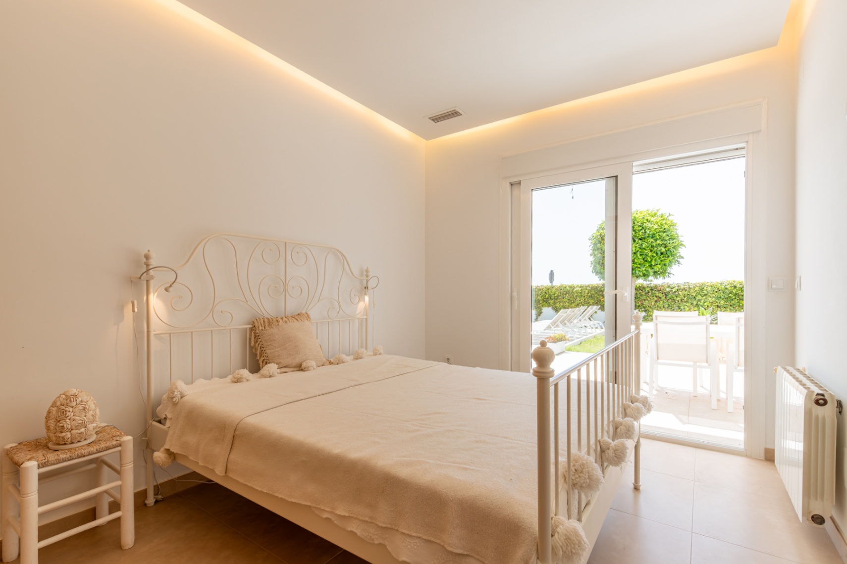 Dormitorio luminoso con cama de hierro forjado, iluminación LED indirecta y acceso directo a una terraza privada con jardín y mobiliario exterior. Dormitorio luminoso con cama de hierro forjado, iluminación LED indirecta y acceso directo a una terraza privada con jardín y mobiliario exterior.