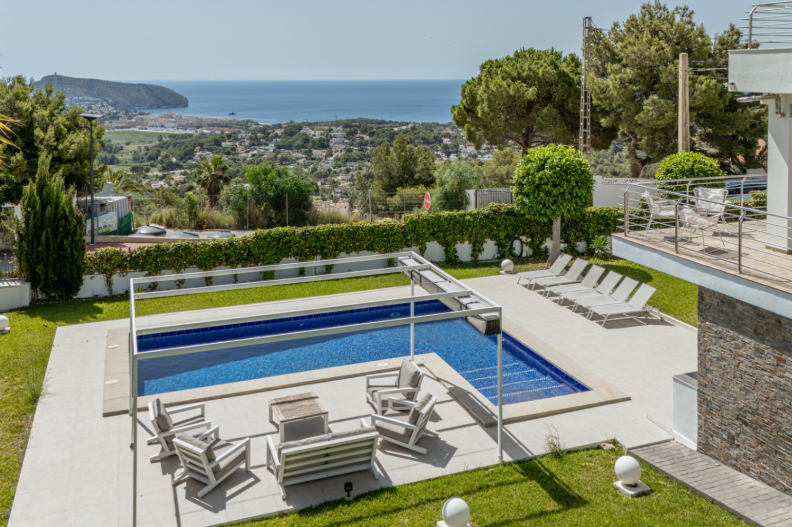 Piscina con cubierta automática y zona chill-out bajo pérgola, en jardín con césped impecable y vistas panorámicas al mar de Moraira. Piscina con cubierta automática y zona chill-out bajo pérgola, en jardín con césped impecable y vistas panorámicas al mar de Moraira.