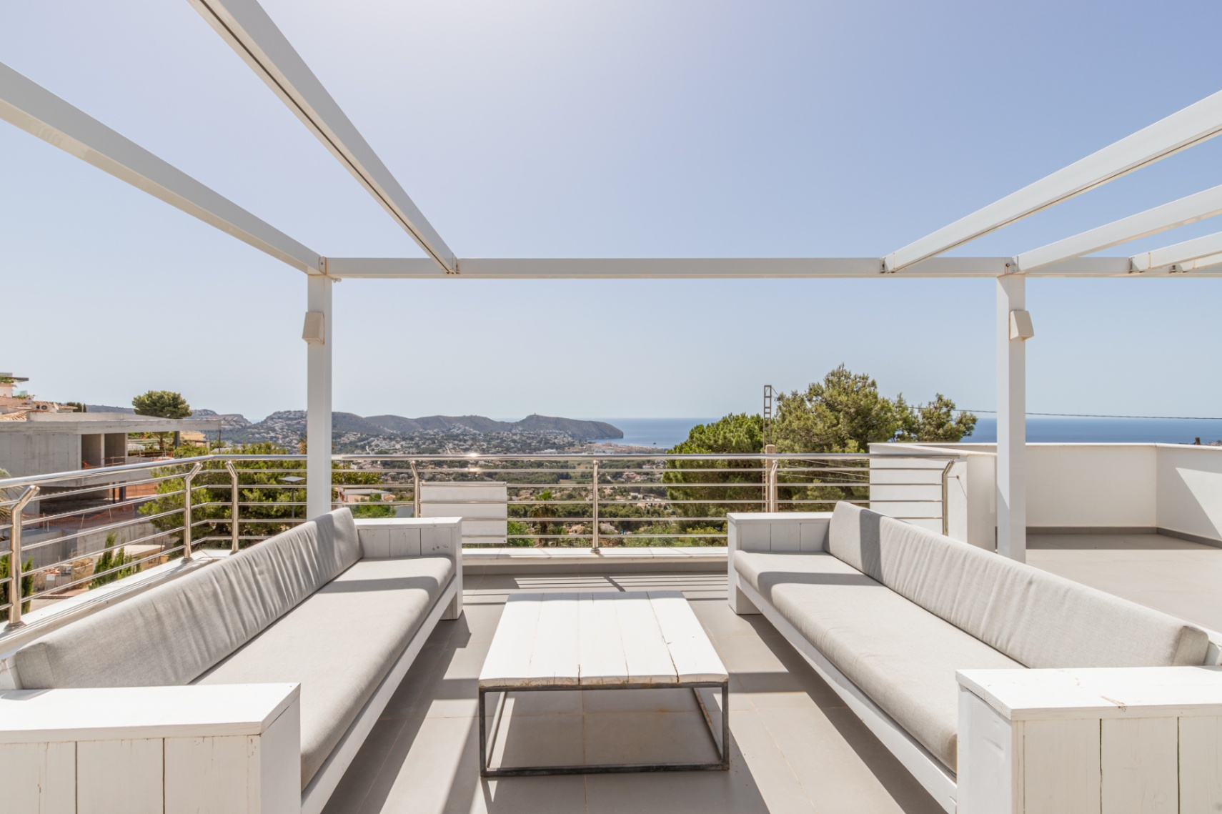 Solárium en la azotea con pérgola blanca, dos sofás exteriores y una mesa de centro, enmarcando vistas panorámicas del mar Mediterráneo y la costa. Solárium en la azotea con pérgola blanca, dos sofás exteriores y una mesa de centro, enmarcando vistas panorámicas del mar Mediterráneo y la costa.