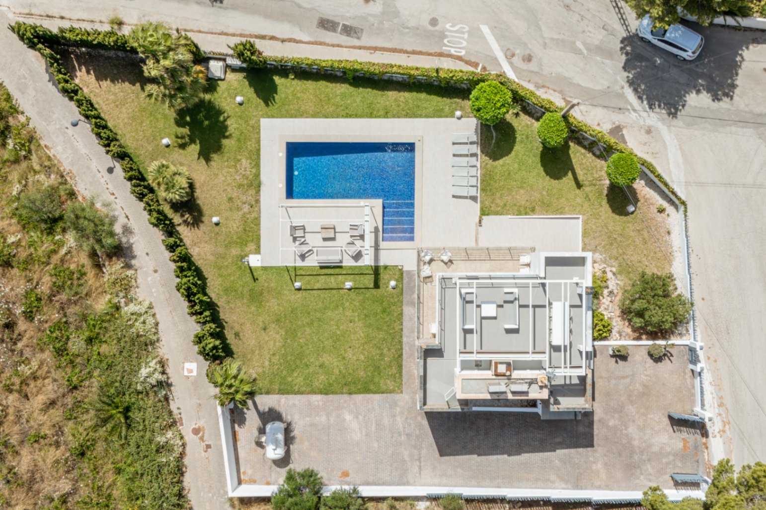 Vista aérea de la propiedad, destacando la piscina rectangular de azulejos azules, el césped impecable y una amplia zona de aparcamiento pavimentada. La cubierta del edificio principal es visible. Vista aérea de la propiedad, destacando la piscina rectangular de azulejos azules, el césped impecable y una amplia zona de aparcamiento pavimentada. La cubierta del edificio principal es visible.