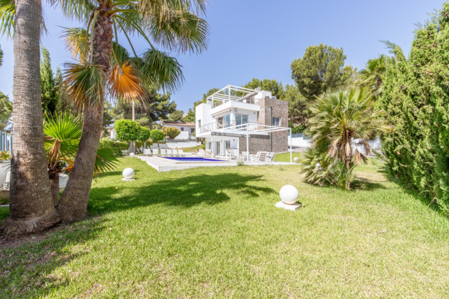 Vista exterior de la villa moderna de varios niveles, con una amplia piscina, césped impecable, palmeras y luces esféricas de jardín. Vista exterior de la villa moderna de varios niveles, con una amplia piscina, césped impecable, palmeras y luces esféricas de jardín.