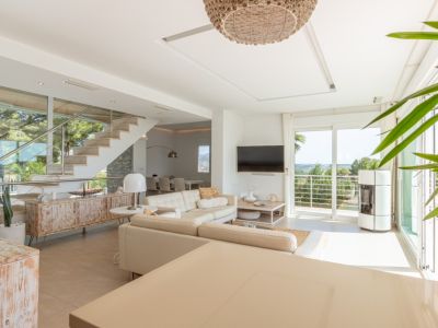 Amplio salón diáfano con sofá crema, estufa de pellets y balcón con vistas. Destacan la escalera de diseño con barandilla de acero y un mueble rústico.