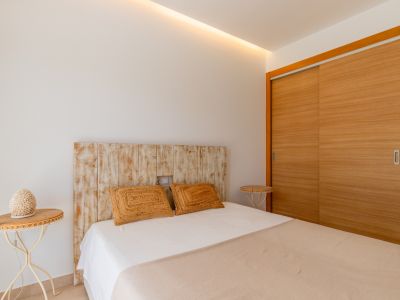 Dormitorio con cabecero de madera envejecida, armario empotrado de puertas correderas de madera clara y luz indirecta en techo.
