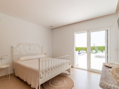 Dormitorio luminoso con cama de forja blanca, suelo cerámico y acceso directo a la terraza exterior con vistas a la piscina.
