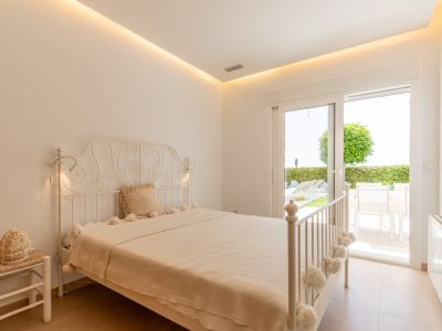 Dormitorio luminoso con cama de hierro forjado, iluminación LED indirecta y acceso directo a una terraza privada con jardín y mobiliario exterior.