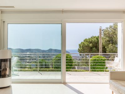 Luminosa zona de día con estufa de pellets y amplios ventanales correderos que acceden a una terraza con vistas al mar y la costa.