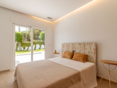 Luminoso dormitorio con cabecero de madera rústica, iluminación de techo integrada y acceso directo a una terraza ajardinada privada mediante puertas correderas.