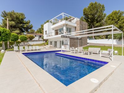Piscina de mosaico azul y terraza pavimentada con zona chill-out bajo pérgola, complementando la moderna villa con fachada de piedra y balcones.