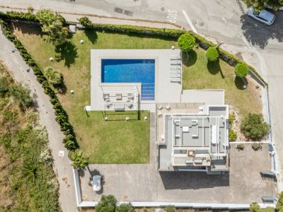 Vista aérea de la propiedad, destacando la piscina rectangular de azulejos azules, el césped impecable y una amplia zona de aparcamiento pavimentada. La cubierta del edificio principal es visible.