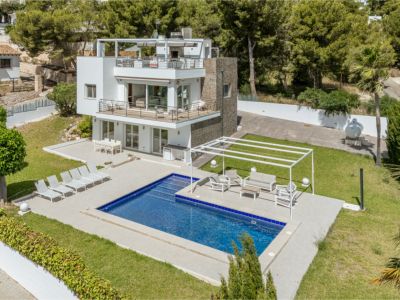Vista aérea de la villa moderna de varios niveles con piscina rectangular, amplias terrazas con zonas de estar y comedor, y césped cuidado, rodeada de exuberante vegetación.