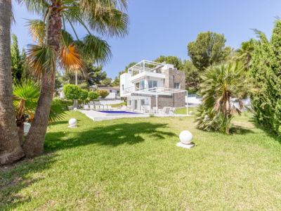 Vista exterior de la villa moderna de varios niveles, con una amplia piscina, césped impecable, palmeras y luces esféricas de jardín.