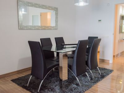Comedor moderno con mesa de cristal y seis sillas de polipiel negra. Destaca el espejo de marco envejecido y el suelo de mármol pulido.