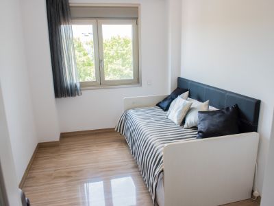 Habitación individual con cama nido, cabecero tapizado negro y ropa de cama a rayas. El suelo de mármol claro pulido y la ventana ofrecen vistas a la vegetación.