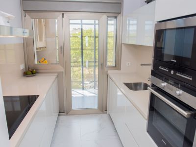 Moderna cocina tipo galera con elegantes muebles blancos, encimeras claras y electrodomésticos Siemens integrados. La puerta doble acristalada proporciona luz natural y acceso a un balcón.