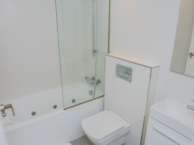 Moderno cuarto de baño blanco con bañera de hidromasaje, mampara de cristal, inodoro suspendido y lavabo rectangular. Azulejos blancos y grifería cromada.
