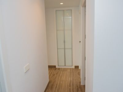Pasillo interior con paredes blancas y suelo de mármol veteado. Al fondo, un armario empotrado de puertas de cristal esmerilado con marco plateado y luz cenital.