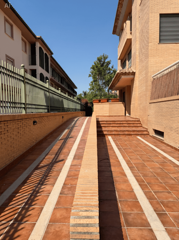 Acceso exterior con rampa de entrada al garaje subterráneo y escaleras a la entrada principal. Suelo de baldosas de terracota con franjas claras y muros de ladrillo. Acceso exterior con rampa de entrada al garaje subterráneo y escaleras a la entrada principal. Suelo de baldosas de terracota con franjas claras y muros de ladrillo.