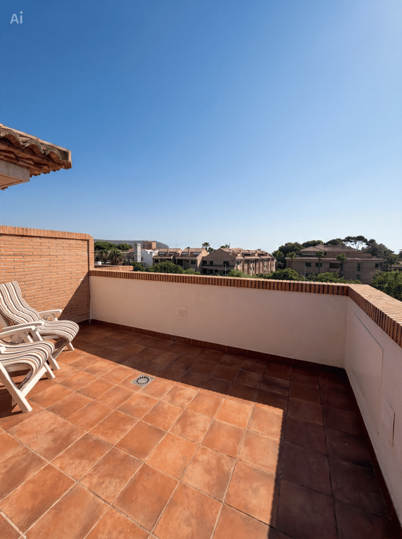 Amplia terraza exterior con suelo de terracota y paredes de ladrillo visto, equipada con dos sillas plegables. Ofrece vistas despejadas a la zona residencial y vegetación bajo un cielo azul. Amplia terraza exterior con suelo de terracota y paredes de ladrillo visto, equipada con dos sillas plegables. Ofrece vistas despejadas a la zona residencial y vegetación bajo un cielo azul.