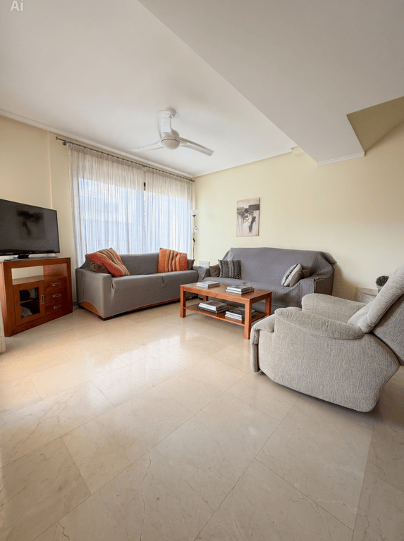 Amplio salón con suelo de baldosas claras efecto mármol, dos sofás confortables, un sillón reclinable y mesa de centro de madera. Luz natural a través del gran ventanal con cortinas translúcidas. Amplio salón con suelo de baldosas claras efecto mármol, dos sofás confortables, un sillón reclinable y mesa de centro de madera. Luz natural a través del gran ventanal con cortinas translúcidas.