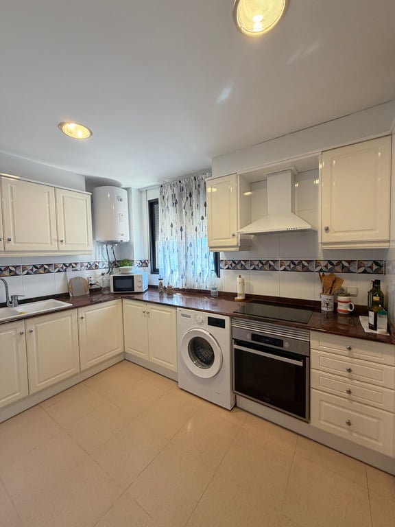 Cocina cerrada con armarios blancos, encimeras granate y electrodomésticos integrados. Incluye lavadora y un calentador de agua mural. Cocina cerrada con armarios blancos, encimeras granate y electrodomésticos integrados. Incluye lavadora y un calentador de agua mural.