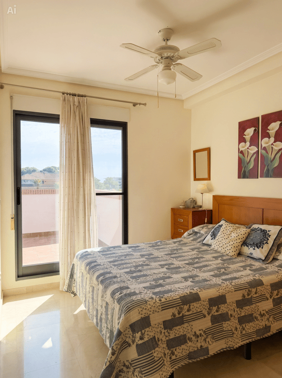 Dormitorio luminoso con cama doble, cabecero de madera y acceso directo a una terraza exterior. Cuenta con ventilador de techo y suelo de baldosas claras. Dormitorio luminoso con cama doble, cabecero de madera y acceso directo a una terraza exterior. Cuenta con ventilador de techo y suelo de baldosas claras.