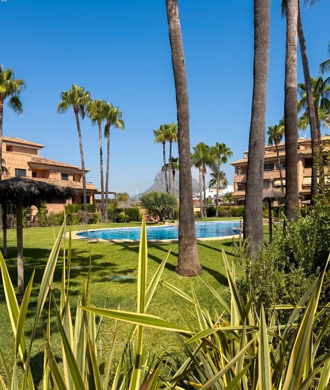 La piscina comunitaria está rodeada por césped verde y altas palmeras, creando un oasis tropical con sombrillas y edificios residenciales al fondo bajo un cielo azul claro. La piscina comunitaria está rodeada por césped verde y altas palmeras, creando un oasis tropical con sombrillas y edificios residenciales al fondo bajo un cielo azul claro.