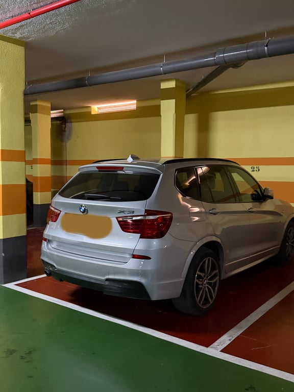 Plaza de garaje privada subterránea con un SUV plateado, paredes amarillas con franjas naranjas y tuberías rojas. Iluminación fluorescente y suelo bicolor. Plaza de garaje privada subterránea con un SUV plateado, paredes amarillas con franjas naranjas y tuberías rojas. Iluminación fluorescente y suelo bicolor.