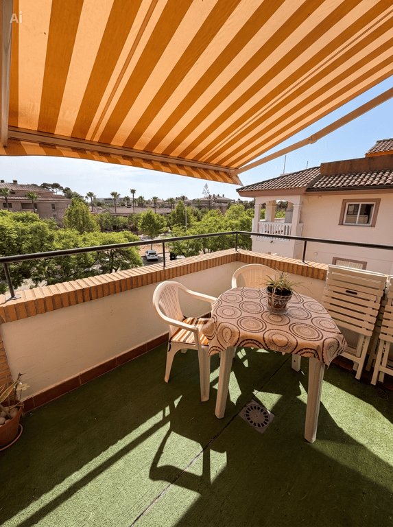 Terraza exterior con césped artificial, mobiliario de plástico y toldo retráctil de rayas. Ofrece vistas a la vegetación y edificios residenciales. Terraza exterior con césped artificial, mobiliario de plástico y toldo retráctil de rayas. Ofrece vistas a la vegetación y edificios residenciales.