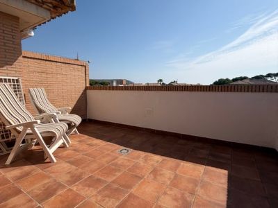 Amplia terraza superior con suelo de baldosas de terracota y pared de ladrillo. Equipada con dos tumbonas, ofrece un espacio soleado y abierto con vistas despejadas.