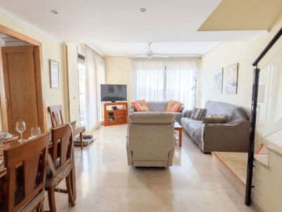 Amplio salón-comedor con suelos de mármol claro, que integra una zona de estar con sofás y un comedor de madera. La estancia recibe luz natural de grandes ventanales y cuenta con aire acondicionado por conductos.