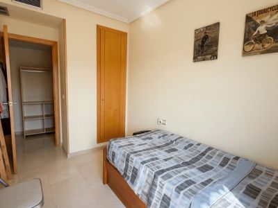 Dormitorio individual con cama de madera, suelo de mármol claro y armario empotrado. Incluye acceso a un vestidor abierto y ventilación de aire acondicionado.