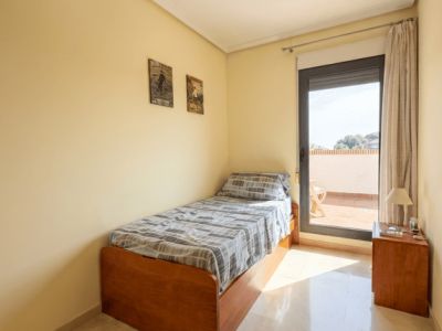 Dormitorio individual con cama de madera, suelo de mármol y acceso directo a una terraza superior, inundado de luz natural.