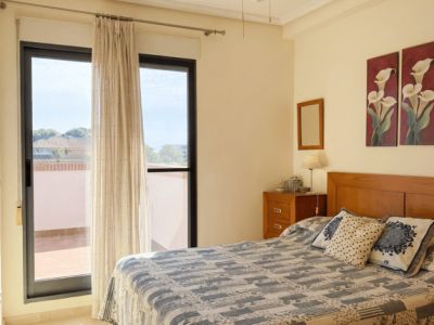Dormitorio luminoso con cama doble, cabecero de madera y acceso directo a una terraza exterior. Cuenta con ventilador de techo y suelo de baldosas claras.