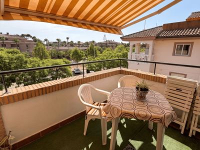 Terraza exterior con césped artificial, mobiliario de plástico y toldo retráctil de rayas. Ofrece vistas a la vegetación y edificios residenciales.