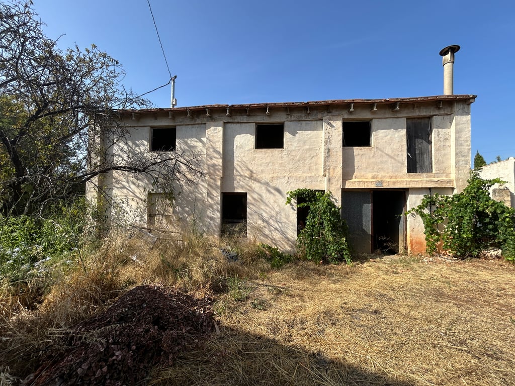 Exterior de una vivienda tradicional de dos plantas con fachada enlucida, múltiples huecos de ventana sin acristalar y una puerta de madera antigua. El tejado y el entorno requieren reforma integral. Exterior de una vivienda tradicional de dos plantas con fachada enlucida, múltiples huecos de ventana sin acristalar y una puerta de madera antigua. El tejado y el entorno requieren reforma integral.