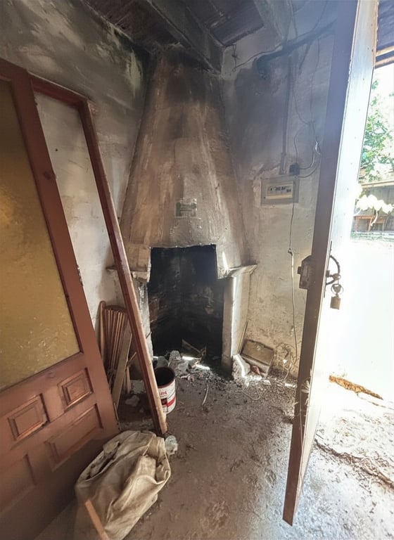 Interior en bruto con una chimenea tradicional de obra, paredes sin revestir y suelo con escombros. Se observa una puerta de madera y luz natural, listo para una reforma integral. Interior en bruto con una chimenea tradicional de obra, paredes sin revestir y suelo con escombros. Se observa una puerta de madera y luz natural, listo para una reforma integral.