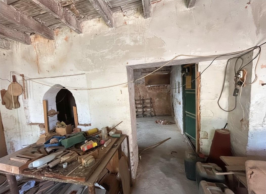 Interior en estado de reforma con vigas de madera expuestas y paredes desconchadas. Destaca un arco decorativo en la pared izquierda y un banco de trabajo desordenado. Interior en estado de reforma con vigas de madera expuestas y paredes desconchadas. Destaca un arco decorativo en la pared izquierda y un banco de trabajo desordenado.