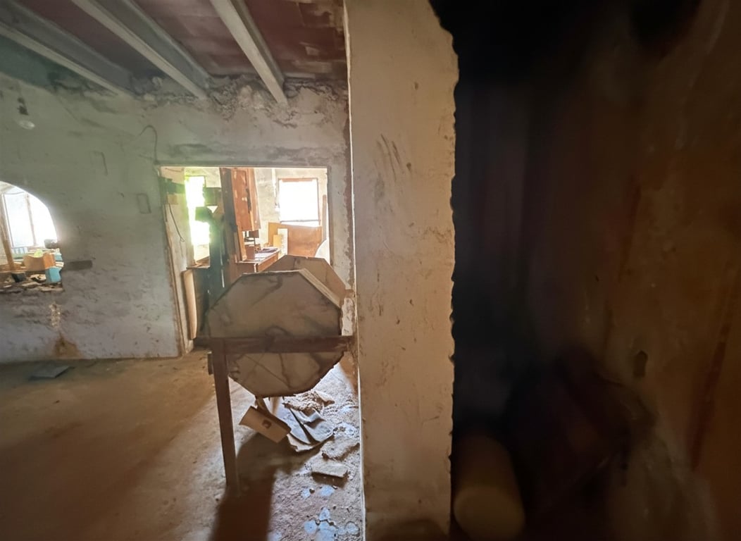 Interior en reforma con vigas de techo expuestas y paredes sin acabar. Una estructura de madera octogonal destaca en el centro, con luz natural al fondo. Interior en reforma con vigas de techo expuestas y paredes sin acabar. Una estructura de madera octogonal destaca en el centro, con luz natural al fondo.