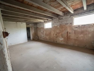 Amplia estancia interior con suelo de hormigón, paredes de ladrillo visto y bloques, y techo con vigas de madera y bovedilla. Dos ventanas pequeñas iluminan el espacio, que requiere reforma integral.
