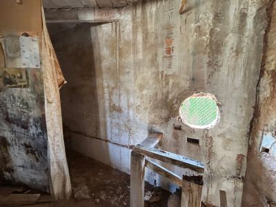 Espacio interior con paredes envejecidas y ladrillo visto, una abertura redonda con malla verde y una estructura de madera rústica. La zona requiere una reforma integral.