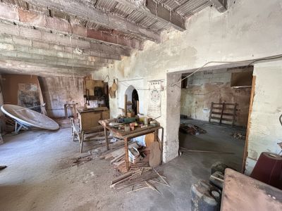 Este espacio interior en bruto muestra vigas de ladrillo y hormigón expuestas, paredes sin revocar y un suelo de hormigón con escombros. Resalta la necesidad de una reforma estructural integral.