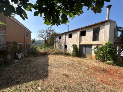 Fachada exterior de la propiedad de dos plantas, con garaje y un amplio jardín privado de tierra rojiza. Requiere reforma integral.