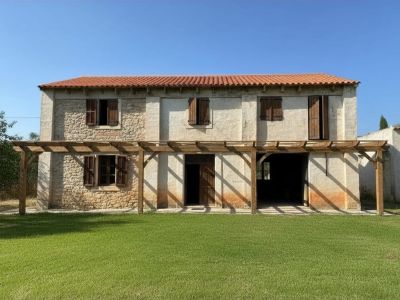 Fachada principal de dos plantas con tejado de teja roja, muros de piedra y enlucidos, y una pérgola de madera sobre el césped.