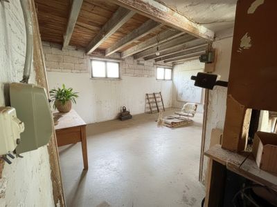Interior diáfano con techo de vigas de madera expuestas y paredes de mampostería. Dos ventanas aportan luz natural a este espacio con suelo de hormigón, listo para reforma.